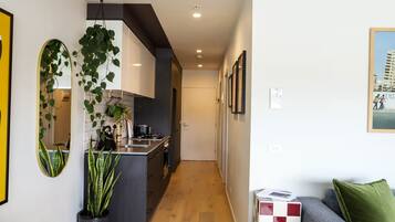 A modern kitchen with a central island, a dining area with a sofa and a green pillow, and a hallway leading to a door.