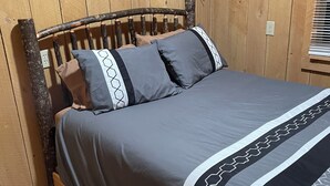 Una cama de madera con cabecera, ropa de cama gris y un estampado geométrico en la falda de la cama.