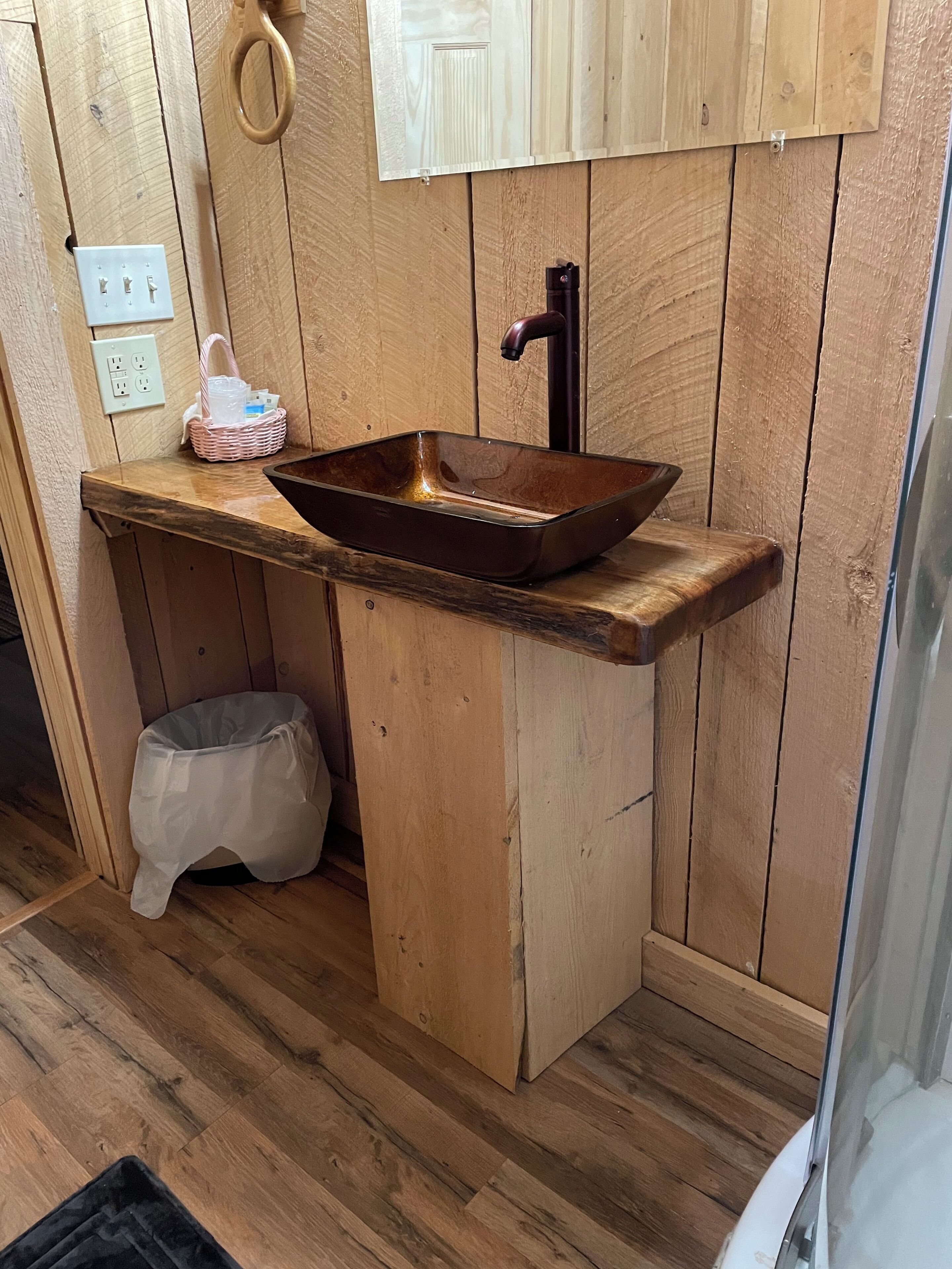 Un baño de madera con un lavabo rectangular, un perchero y una pequeña cesta.