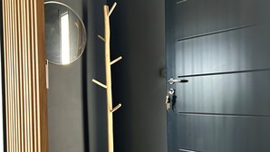A dark-colored door with a keyhole and a handle, a wooden coat rack with hooks, and a round mirror on the wall. - House with breathtaking views over the valley, only 15 minutes from Corte (Poggio-di-Venaco)