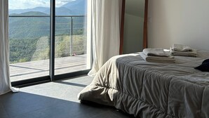 A bedroom with a large bed, a mirror, and a view of mountains through a sliding glass door. - House with breathtaking views over the valley, only 15 minutes from Corte (Poggio-di-Venaco)