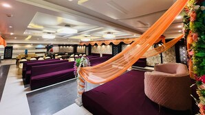 Une salle de banquet avec des sièges violets, une scène centrale et un dais orange drapé.