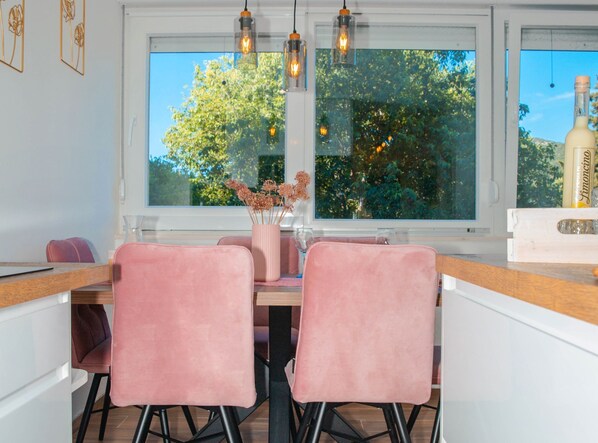 A modern kitchen with two pink chairs, a wooden table, and a large window with a view of trees.