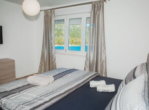 A bedroom with a bed, a window with curtains, a bedside table, and a wall-mounted light fixture. - Apartment Matko (Ploce)