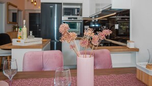 Et moderne køkken med hvide skabe, rustfrie hvidevarer og en lyserød vase med blomster på spisebordet.