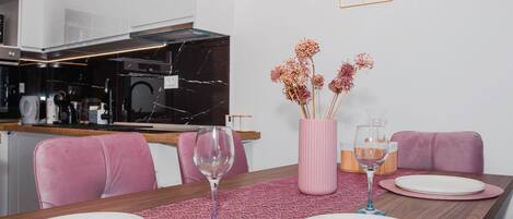 A modern dining area with pink chairs, a wooden table, and a pink vase with flowers.