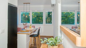 Et kompakt køkken med spiseplads, store vinduer og udsigt til grønne omgivelser.