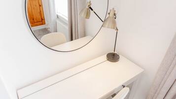 A white vanity with a round mirror and two lamps.