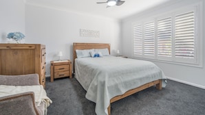 A bedroom with a bed, wooden dresser, nightstands, and a ceiling fan.