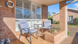 A patio with two chairs and a small table, a brick wall, and a window with shutters.