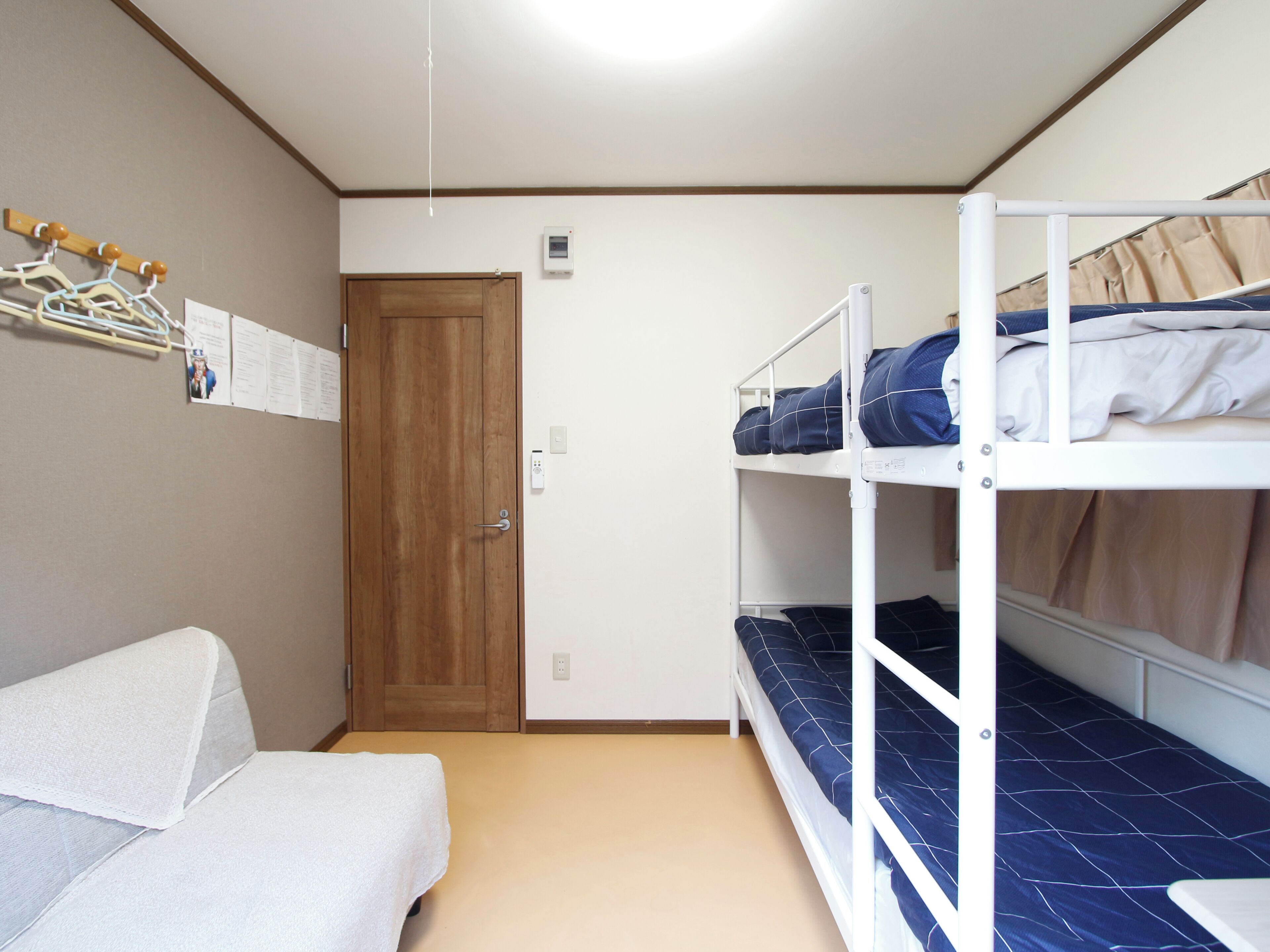 A dormitory room with bunk beds, a wooden door, a coat rack, and a bulletin board.