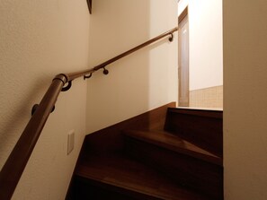 Een houten trap met een leuning en een lichtschakelaar aan de muur.