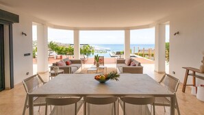 A spacious dining area with a view of the ocean, a pool, and outdoor seating.