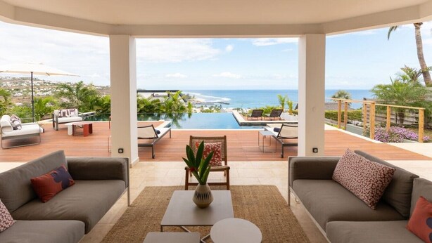 A spacious living area with a view of the ocean, a pool, and outdoor seating.
