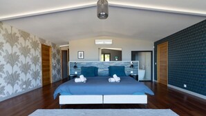 A modern bedroom with a large bed, a nightstand, a bedside table, a mirror, and a bathroom visible through an open door. - Luxueuse Villa Calypso - Piscine et vue mer à Saint Gilles les Bains (Saint Gilles les Bains)