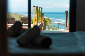 Un letto con cuscini, vista sull'oceano e un pontile in legno con sedie.