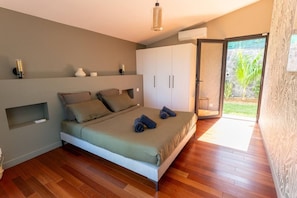 Ein Schlafzimmer mit Bett, Schrank, einer kleinen Ablagefläche und einer Schiebeglastür zu einem Außenbereich.