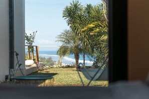 Vista da interno verso un balcone con una palma e l'oceano.