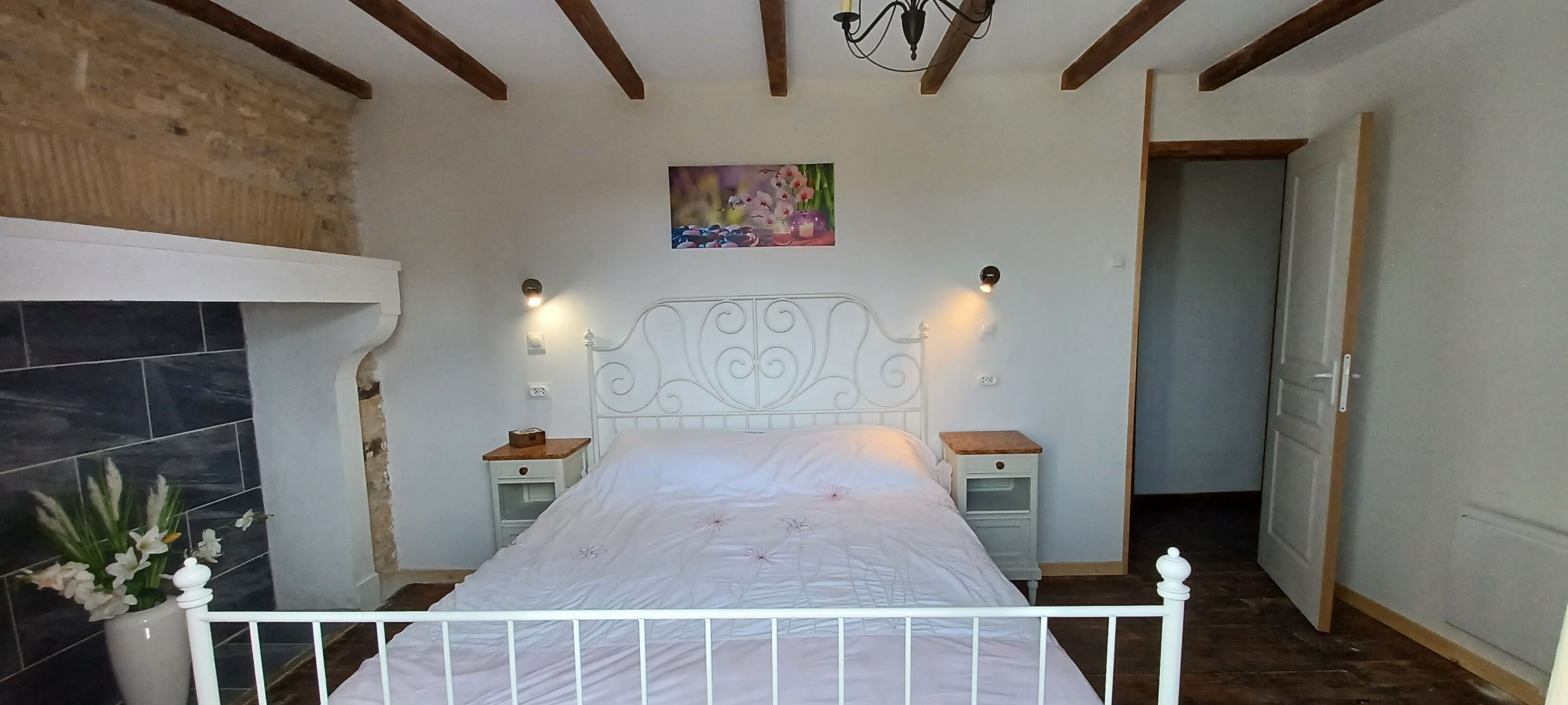 Una camera da letto con un letto bianco, due comodini, una testiera bianca, un quadro appeso al muro e una parete in mattoni su un lato.