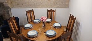 A round wooden dining table set with plates, cutlery, and a vase of flowers.
