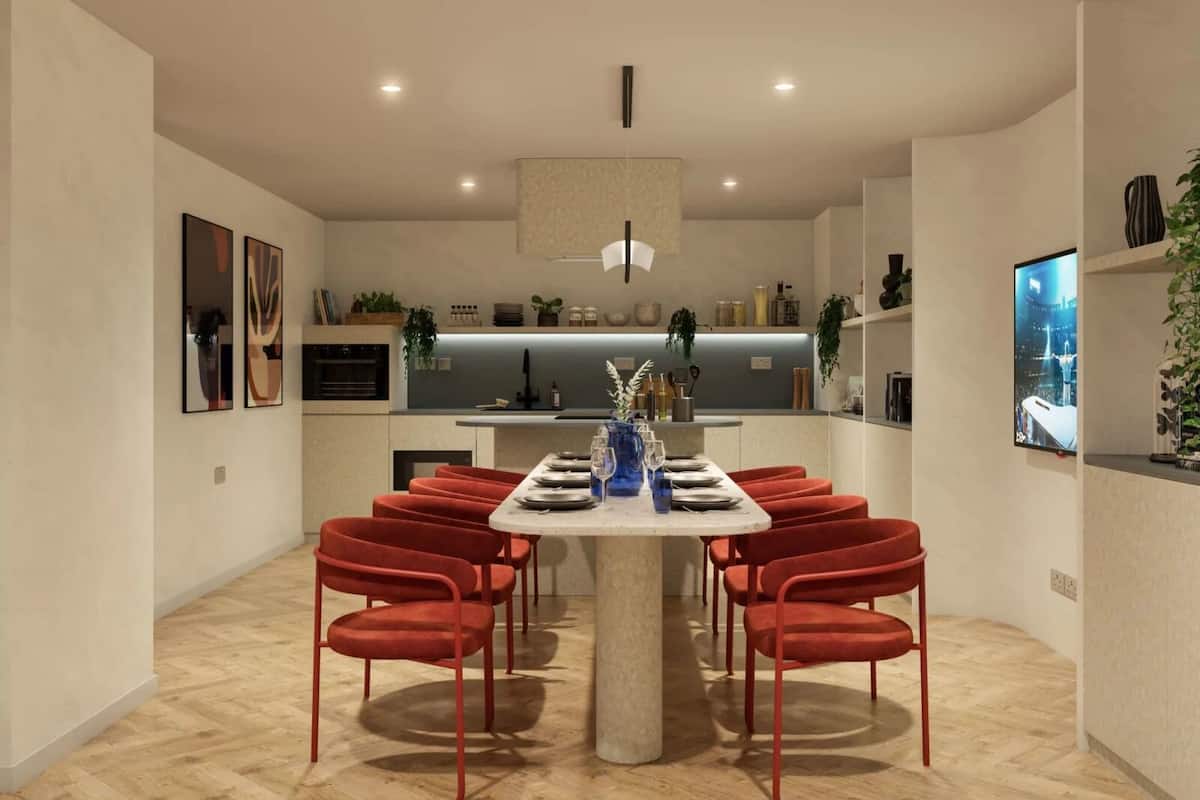 A modern dining area with a round table, red chairs, and a kitchen in the background.