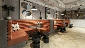 Een modern interieur met een zithoek met gestoffeerde banken en ronde tafels, een houten visgraatvloer en kunstwerken aan de wanden.