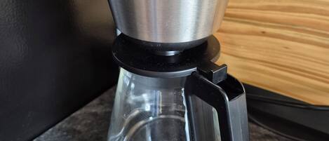 Une cafetière en acier inoxydable avec un manche noir et une verseuse en verre, posée sur un plan de travail.