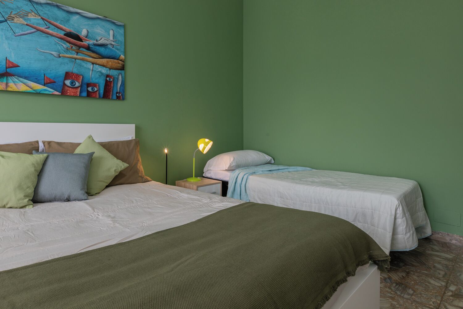 A room with a large bed, a smaller bed, green walls, and a painting above the larger bed.
