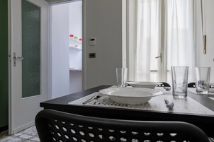Zona pranzo con tavolo apparecchiato per due, un piatto bianco, due bicchieri trasparenti e una sedia nera.