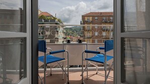 A balcony with two blue chairs and a small table, overlooking a residential area with buildings and a mountainous backdrop. - CasaTo by Wonderful Italy (Turin)