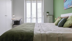 A bedroom with a bed, a desk, a chair, a radiator, and a window with curtains. - CasaTo by Wonderful Italy (Turin)