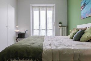 Una camera da letto con un letto, una scrivania, una sedia, un termosifone e una finestra con tende.