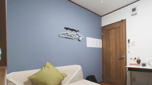 Een slaapkamer met een bed, een houten deur, een klein tafeltje met toiletartikelen en een kapstok aan de muur.