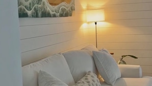 A white sofa with patterned cushions, a wall-mounted lamp, and a wooden accent piece. - Beachside Modern Wellness Villa with Spacious Patio, Walk to the Beach (Jupiter)
