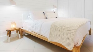 A minimalist bedroom with a wooden bed, white bedding, and a bedside table with a lamp. - Beachside Modern Wellness Villa with Spacious Patio, Walk to the Beach (Jupiter)
