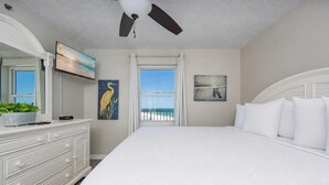 Un dormitorio con una cama grande, ventilador de techo, cómoda, televisor y obras de arte.