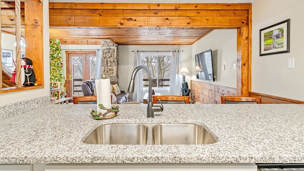 A kitchen with granite countertops, a stainless steel sink, wooden beams, a stone wall, and a dining area with a table and chairs. - 3 Bed, 2 Bath in Seven Springs Resort (Champion)