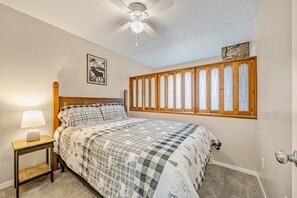Ein Schlafzimmer mit einem Bett, einem Nachttisch mit Lampe, einem Deckenventilator und einem Fenster mit farbigen Glasflächen.