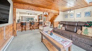 A cozy living room with a brown leather sofa, wooden coffee table, and a kitchen area with white cabinets and a dining set. - 3 Bed, 2 Bath in Seven Springs Resort (Champion)