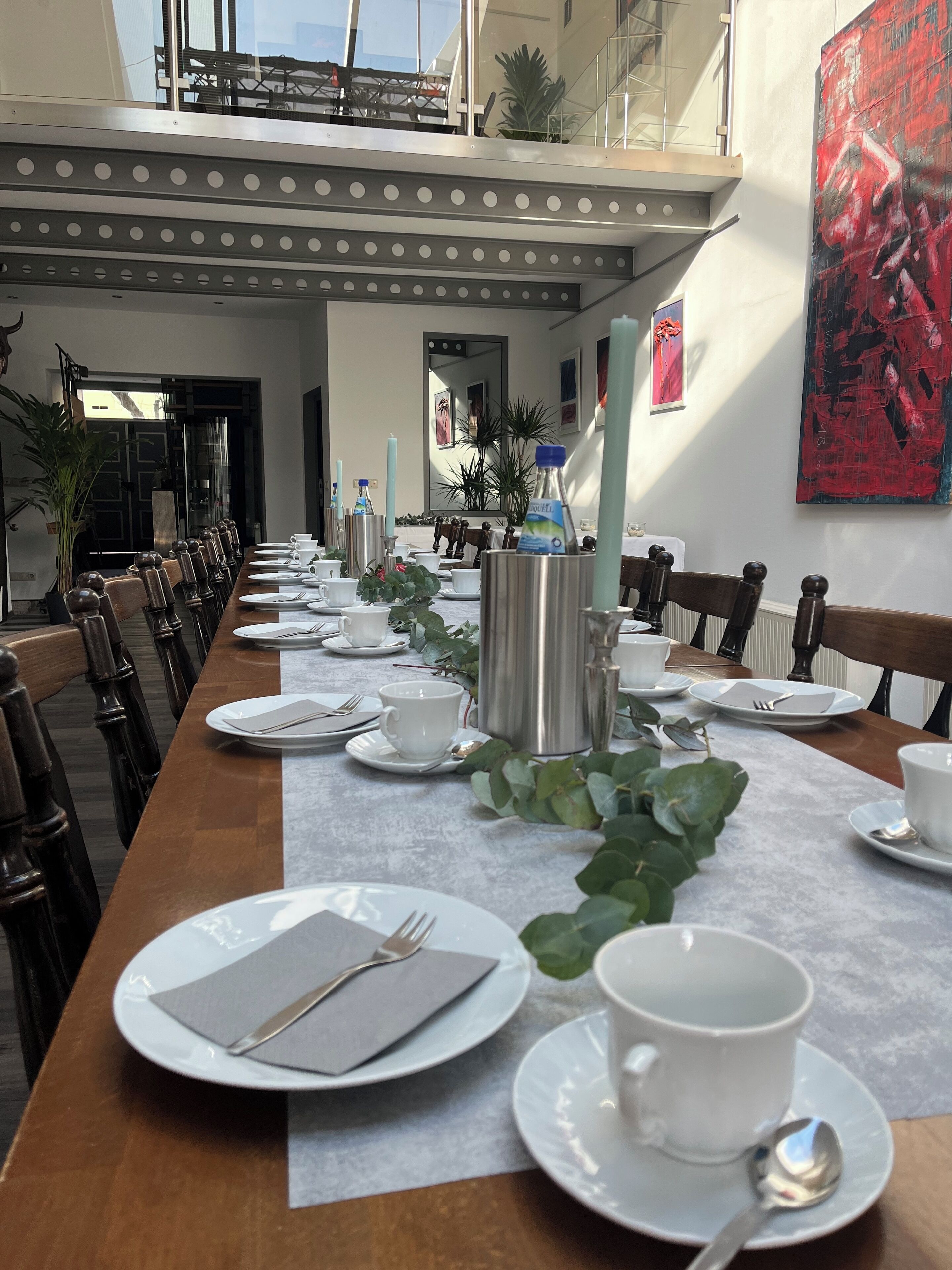 A long dining table set for a meal with white plates, cups, and cutlery, surrounded by chairs.