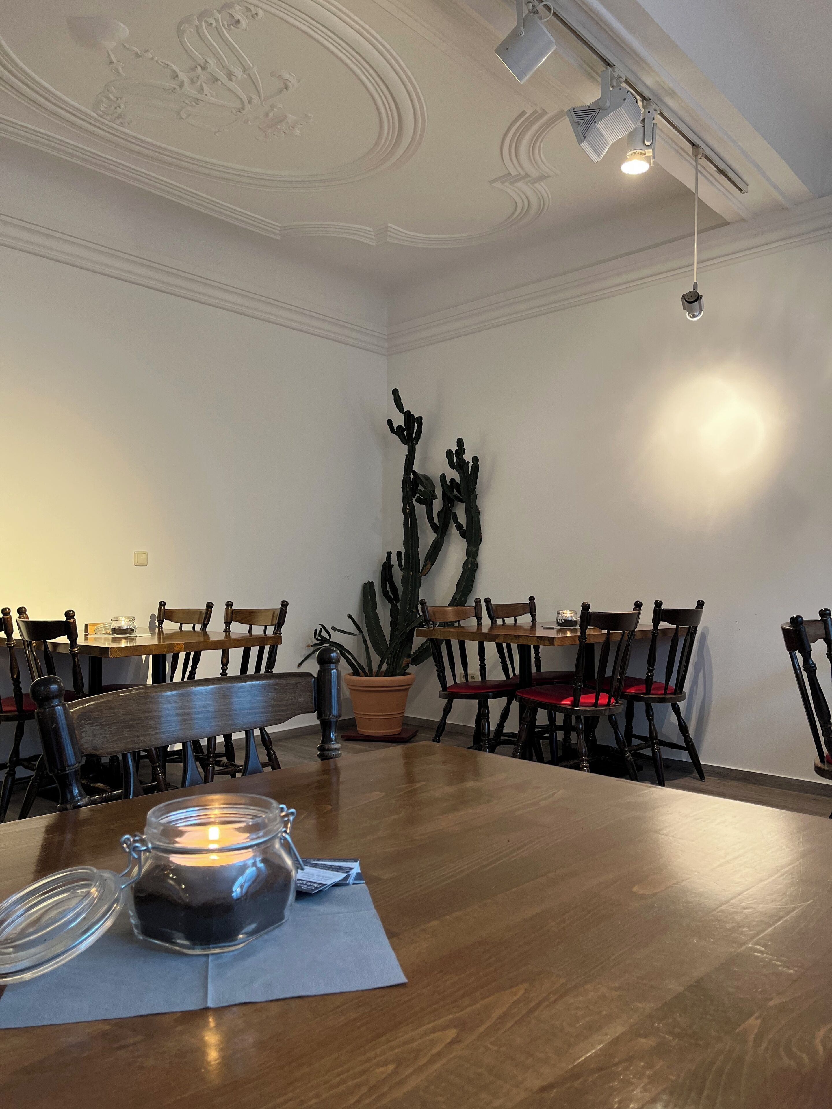 A dining area with wooden tables and chairs, a cactus plant, and a candle on the table.