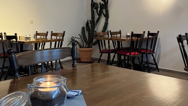 Un comedor con mesas y sillas de madera, una planta de cactus y una vela sobre la mesa.