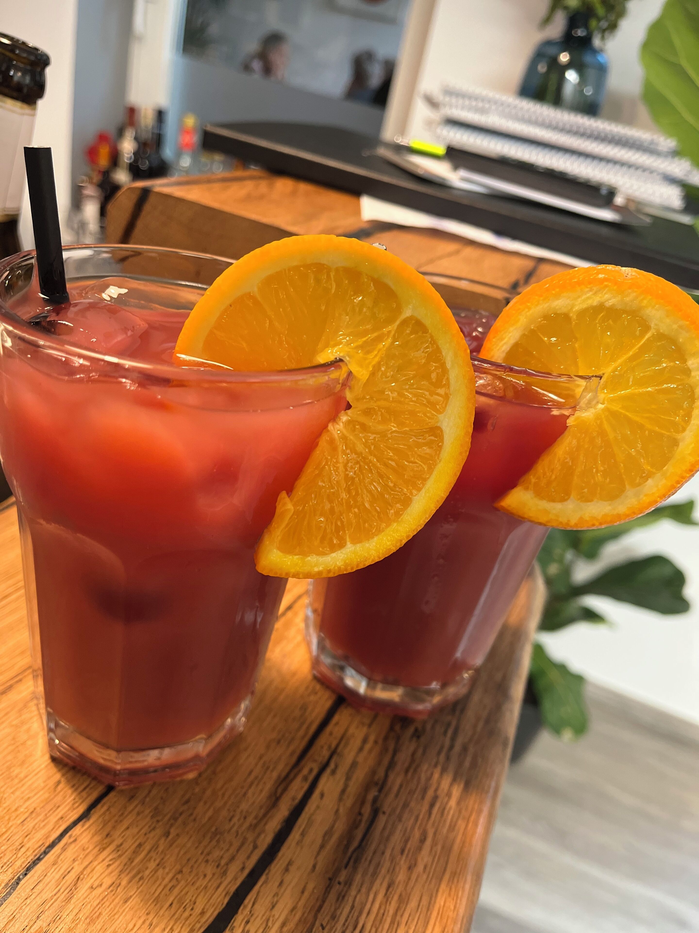 Two glasses of red beverage with orange slices on a wooden surface.