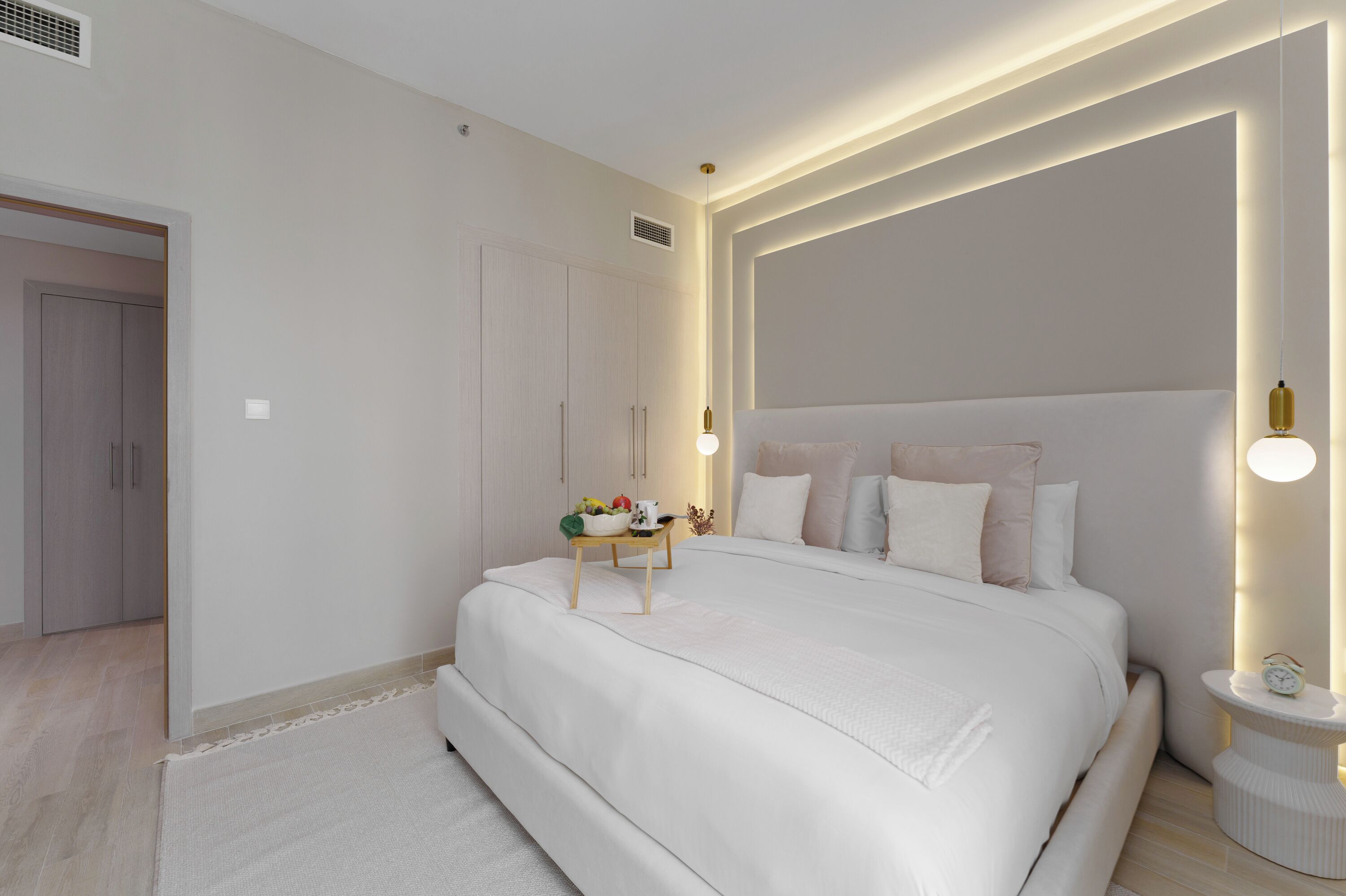 A modern bedroom with a large bed, bedside table, and a nightstand with a lamp.