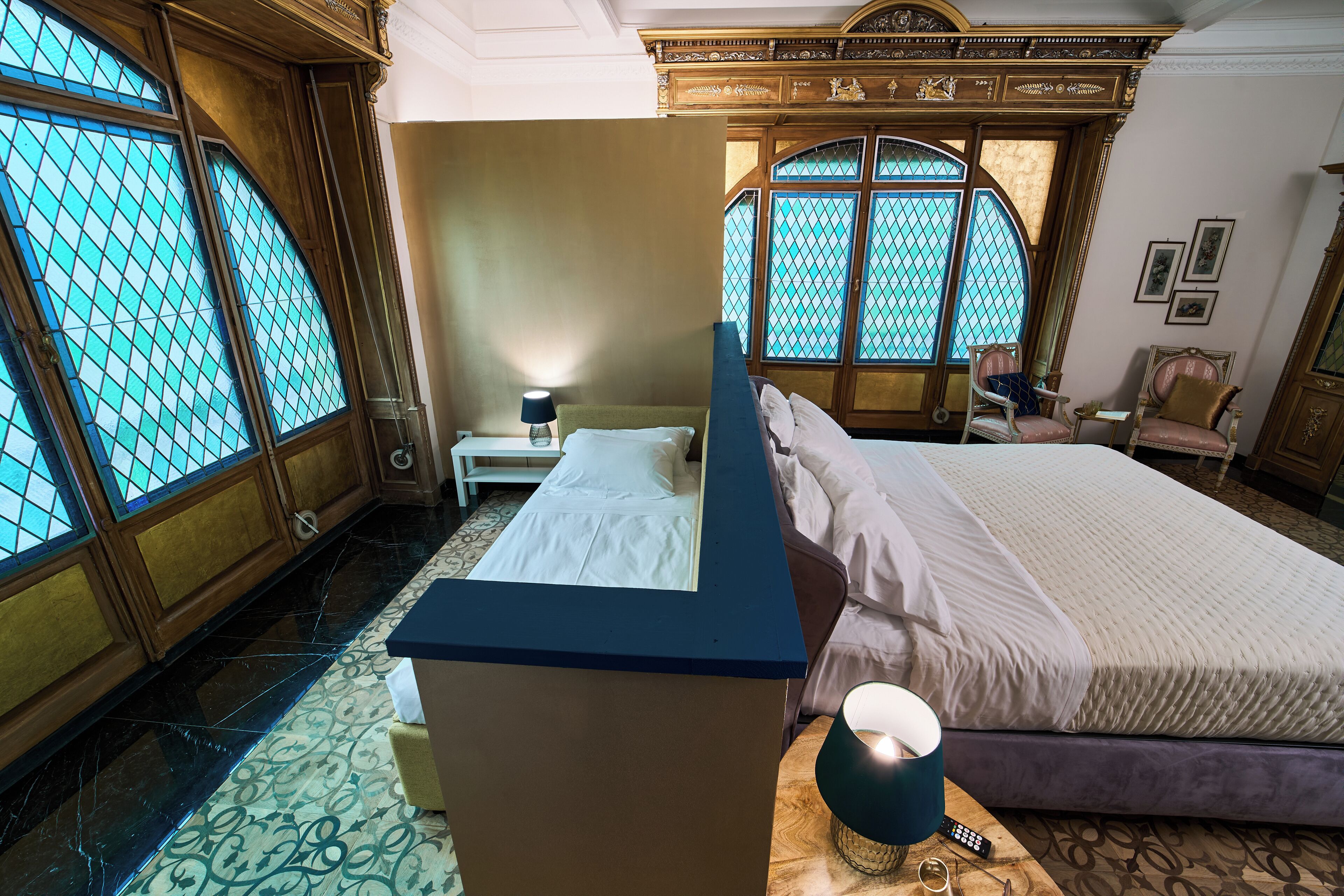 Une chambre à coucher avec un grand lit, une table de chevet, une commode et une fenêtre ornée de vitraux.
