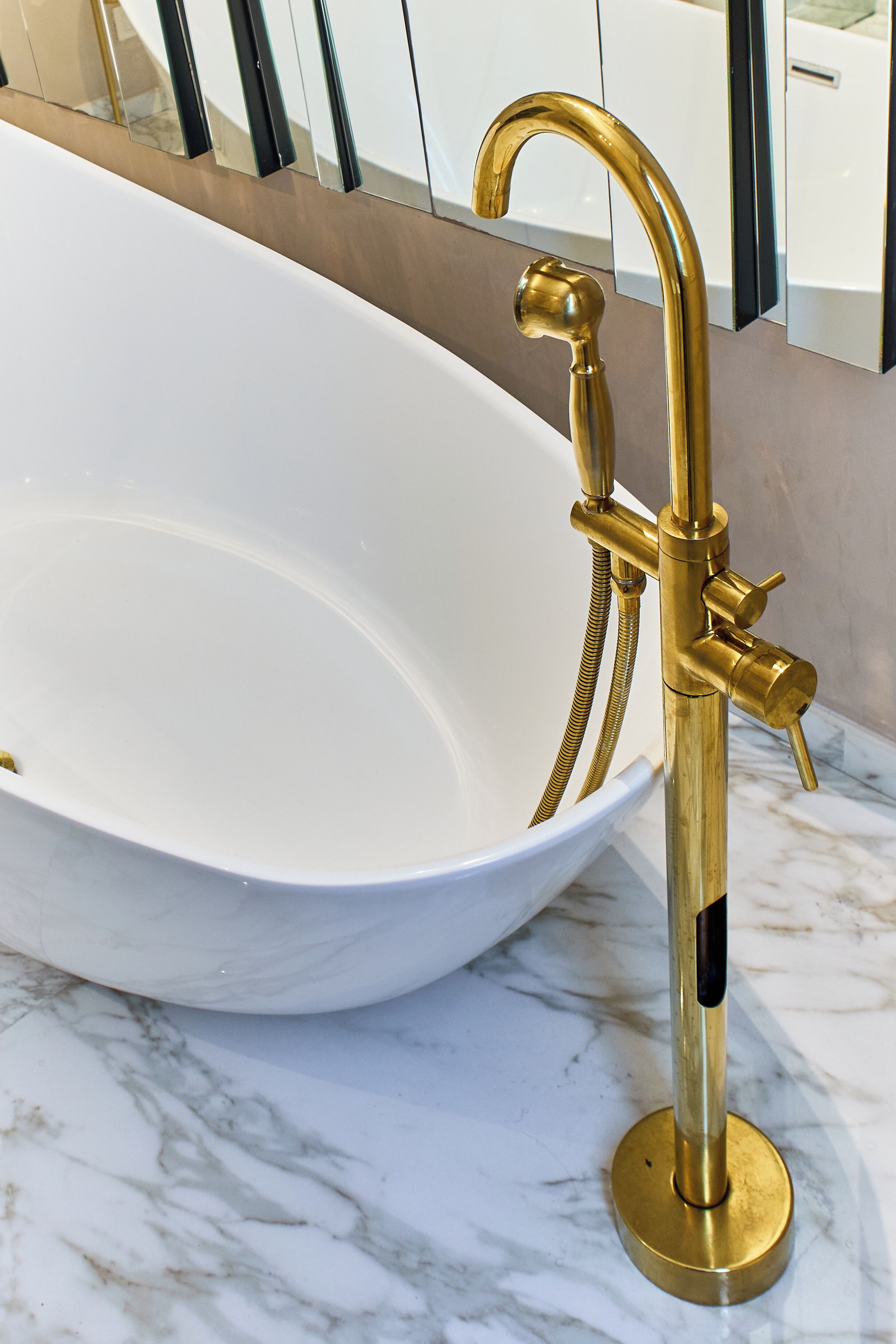 A bathtub with a gold faucet and hose, set on a marble floor.