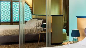 Ein Hotelzimmer mit Bett, Nachttisch, Lampe und Blick durch ein Fenster mit dekorativem Sichtschutz.