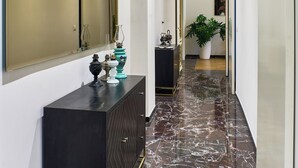 A hallway with a marble floor, a large mirror, a potted plant, and a dark-colored cabinet. - GLAM TIME (Genoa)
