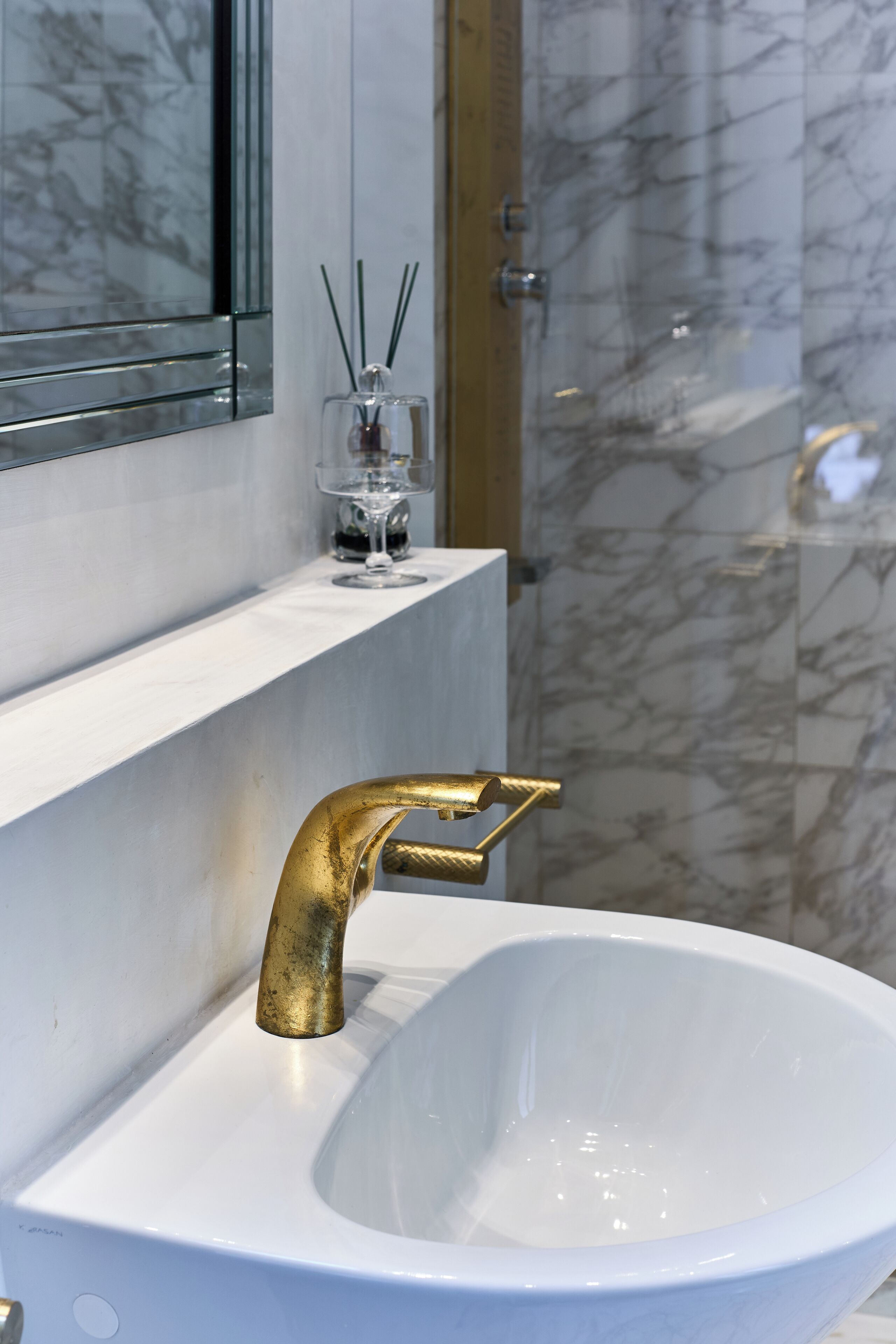 Ein Badezimmer mit einem weißen Waschbecken, einem goldenen Wasserhahn und Marmorwänden.