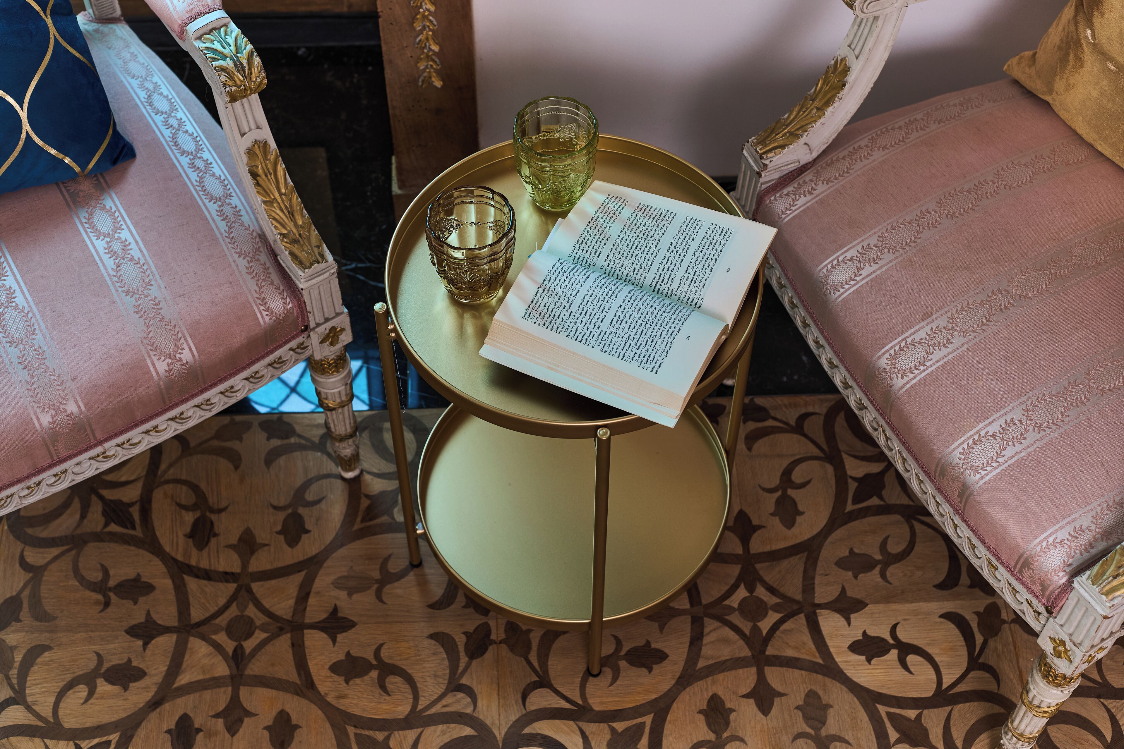 Een kamer met een ronde tafel, twee stoelen, een boek en twee glaasjes.